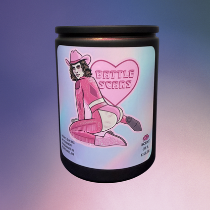 Candle with a label featuring a cowboy in pink attire and 'Battle Scars' text on a gradient background